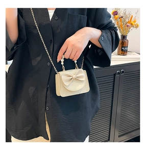 Close-up of mini crossbody bag with pearl handle, ribbon bow and gold chain strap detail
