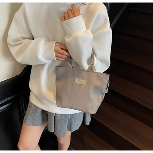 Close-up of a grey nylon tote bag with Fashion label held by a model on stairs