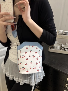 Chic bucket bag with cherry print and blue trim featuring a geometric woven shoulder strap