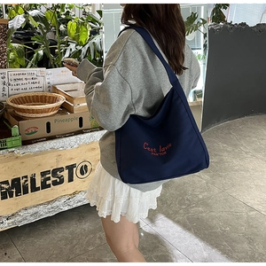 Detail of navy canvas crescent tote bag with red embroidery in a vintage cafe setting
