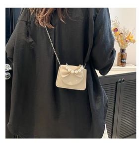Detail of mini crossbody bag with bow and pearl handle on model in black outfit