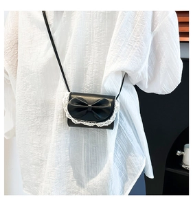 Close-up of sweet style black shoulder bag featuring a large bow and white lace trim detail