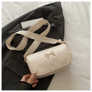 Détail du sac à main carré beige avec nœud doré et large bandoulière en tissu amovible
