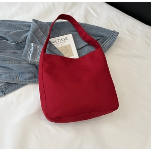 Detail of red canvas tote bag on white bedsheets with artistic cards and denim jacket