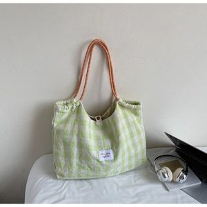 Detail of green and white checkered tote bag featuring orange braided rope handles and logo