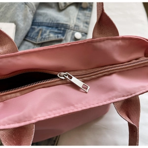 Detail of pink nylon tote bag featuring silver metal zipper and woven webbing strap
