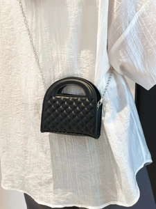 Modern black quilted crossbody bag with silver chain strap shown on model in white outfit