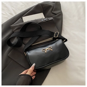 Détail du sac bandoulière noir avec nœud en métal doré et large bandoulière en tissu