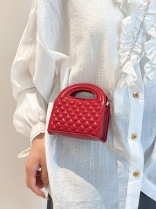 Red quilted mini handbag with silver chain strap shown on a white textured blouse