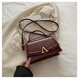Detail of burgundy textured tote bag with golden V-shaped clasp and adjustable strap