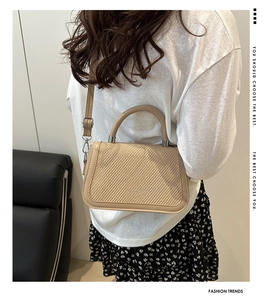 Détail du sac beige avec rabat à texture tissée et boucles métalliques de sangle