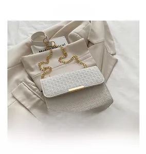 Détail du sac tissé blanc avec fermoir doré posé sur un costume beige et tissu blanc