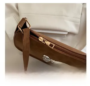 Détail d'une fermeture éclair dorée et nœud argenté sur un sac porté épaule marron