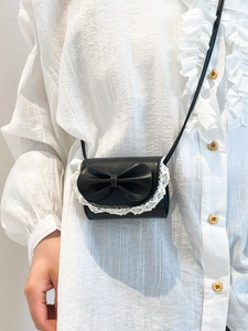 Sac bandoulière en cuir noir avec nœud et dentelle porté sur une blouse blanche