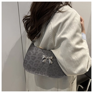 Détail du sac sous le bras à motif léopard gris avec un nœud papillon argenté sur l'épaule