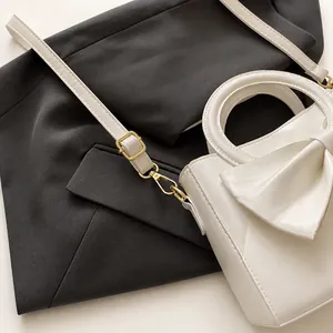 Detailed macro view of gold-tone metal hardware and bow design on white leather bag