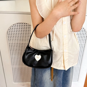 Detail of black faux leather handbag featuring a heart patch and golden bow accent