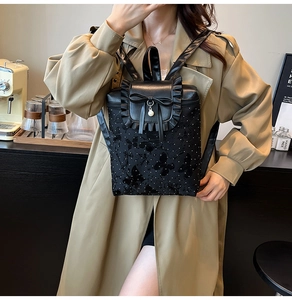 Detail of black backpack featuring lace ruffles, silk bows, and a pearl pendant charm