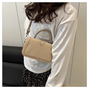 Détail du sac carré beige en paille tressée avec bordure en cuir et poignée supérieure