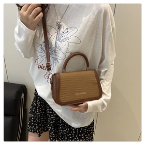 Détail d'un sac bandoulière marron avec texture tissée et poignée supérieure incurvée