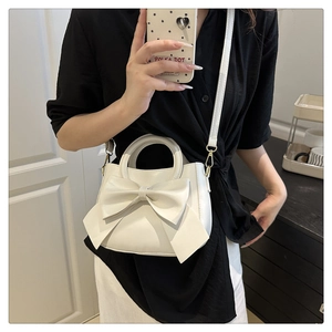 Detailed view of white crossbody bag with oversized bow and golden hardware