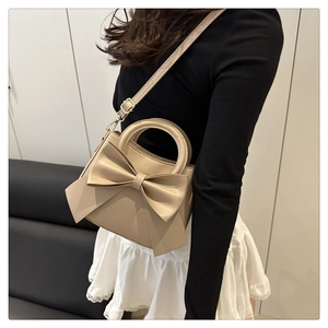 Beige crossbody bag with bow detail shown on a model with black top and white skirt