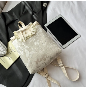 Macro view of butterfly patterns and ruffles on this cream faux leather backpack
