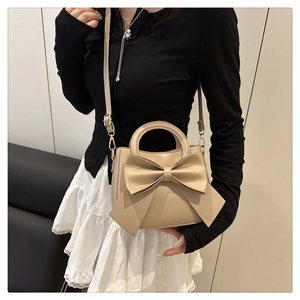Detail of a beige bow handbag featuring a pearl pendant and metal strap clips on a model
