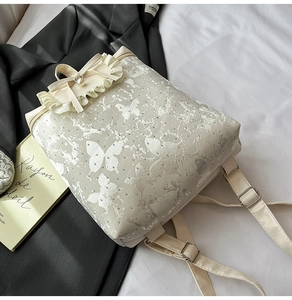 Detail of ruffled flap backpack featuring gray butterfly print and pearl buckle accent