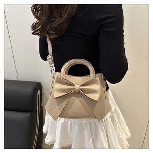 Detail of a beige crossbody bag with a large stylish 3D bow and golden hardware