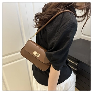Sac bandoulière en similicuir marron foncé avec boucle dorée porté par un modèle