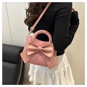 Detailed view of pink shoulder bag featuring a large bow and round handle on a model