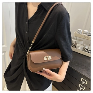 Close-up of brown crossbody bag with gold buckle and chain strap on a black shirt