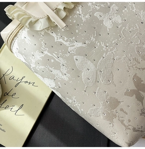 Detailed macro view of cream ruffled handbag featuring butterfly prints and silver rivets