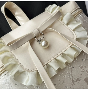 Close-up of cream ruffles, bow, and pearl pendant on a jacquard texture backpack