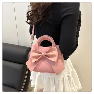 Pink handbag with large bow detail and adjustable shoulder strap shown on model