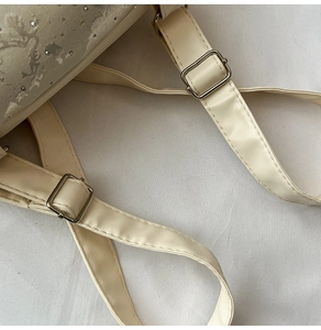 Close-up of adjustable faux leather straps and silver metal buckles on a cream backpack