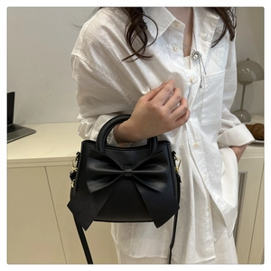 Detail of elegant black handbag featuring a large stylish bow and matte leather finish
