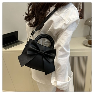 Detail of elegant black PU leather handbag with large bow and gold metal hardware