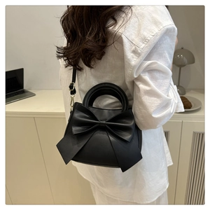 Detail of elegant black leather handbag with a large 3D bow and gold metal hardware hooks