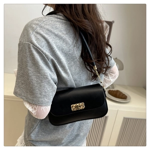 Detail of elegant black shoulder bag featuring a gold buckle on minimalist strap