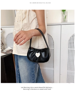 Detail einer Mini-Handtasche aus schwarzem Kunstleder mit weißem Herz und goldener Schleife