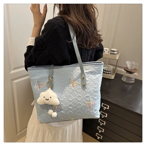 Detail of light blue quilted tote bag featuring butterfly embroidery and plush charm