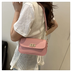 Detail view of a pink crossbody bag with gold twist lock and chain strap on a model