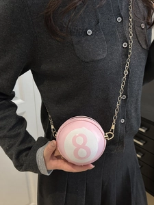 Sac bandoulière sphérique rose avec numéro 8 et chaîne dorée porté par un mannequin