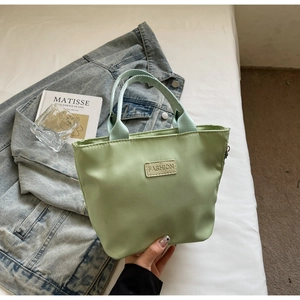 Close-up of a light green nylon handbag with a FASHION leather patch on white bedding