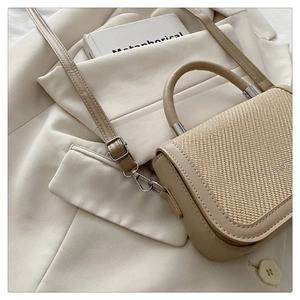 Détail du sac à main bicolore en paille et similicuir sur une veste de costume blanche