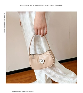 Detail der beigen minimalistischen Handtasche mit Herz-Schleifen-Metallanhänger und Reißverschluss