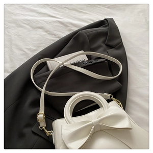 Detail of white leather handbag featuring a large bow and gold-tone metal hardware strap