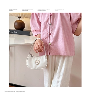 Detail einer weißen herzförmigen Handtasche mit Strassschleife, gehalten von einem Modell